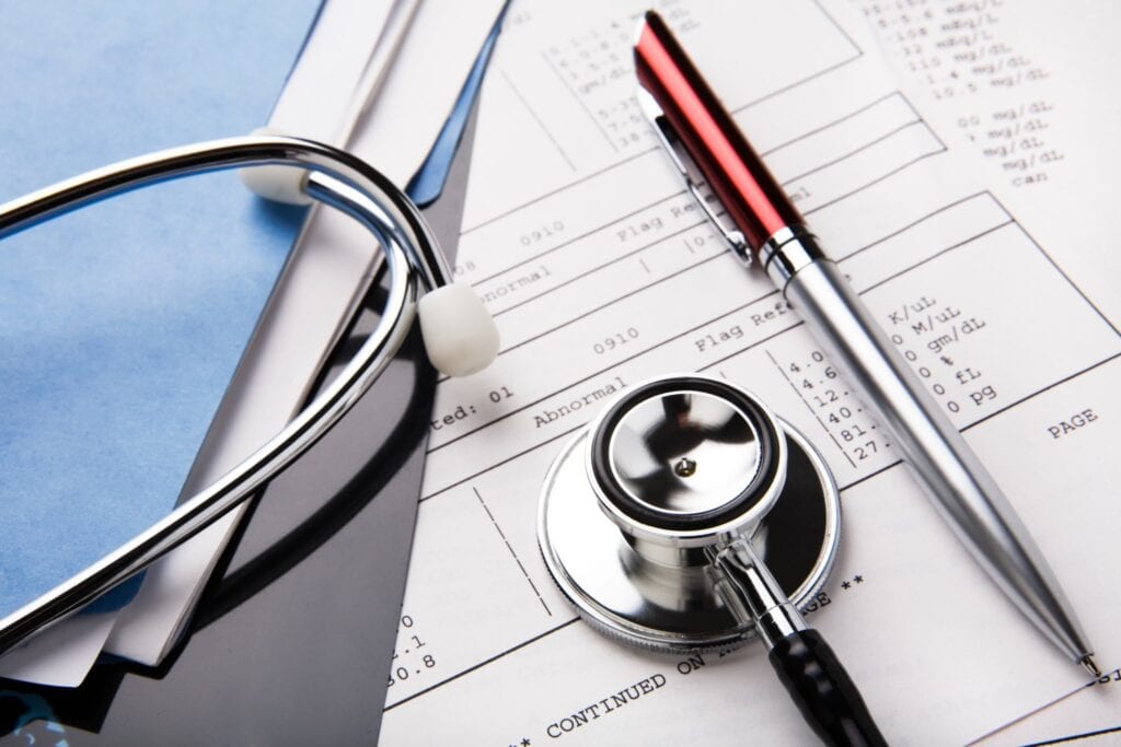 "stethoscope and pen resting on a sheet of medical lab test results, with patient file and x-ray or mri film"